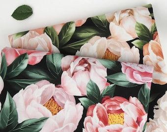 May include: A folded piece of fabric featuring a floral pattern with large, layered pink and peach peony blossoms, dark green leaves, and yellow centers set against a solid black background, accompanied by a single small green leaf.