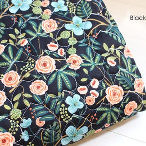 Pu&ograve; includere: Un tessuto trapuntato con sfondo nero e un motivo floreale di rose color pesca, fiori azzurri e fogliame verde scuro. Il tessuto presenta un motivo a griglia cucito in bianco e il testo Black Blossom nell'angolo.