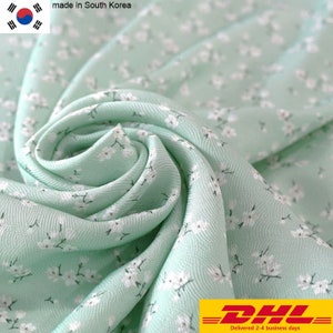 May include: A close-up of a light green fabric with a white floral pattern. The fabric is made in South Korea and is being shipped by DHL.