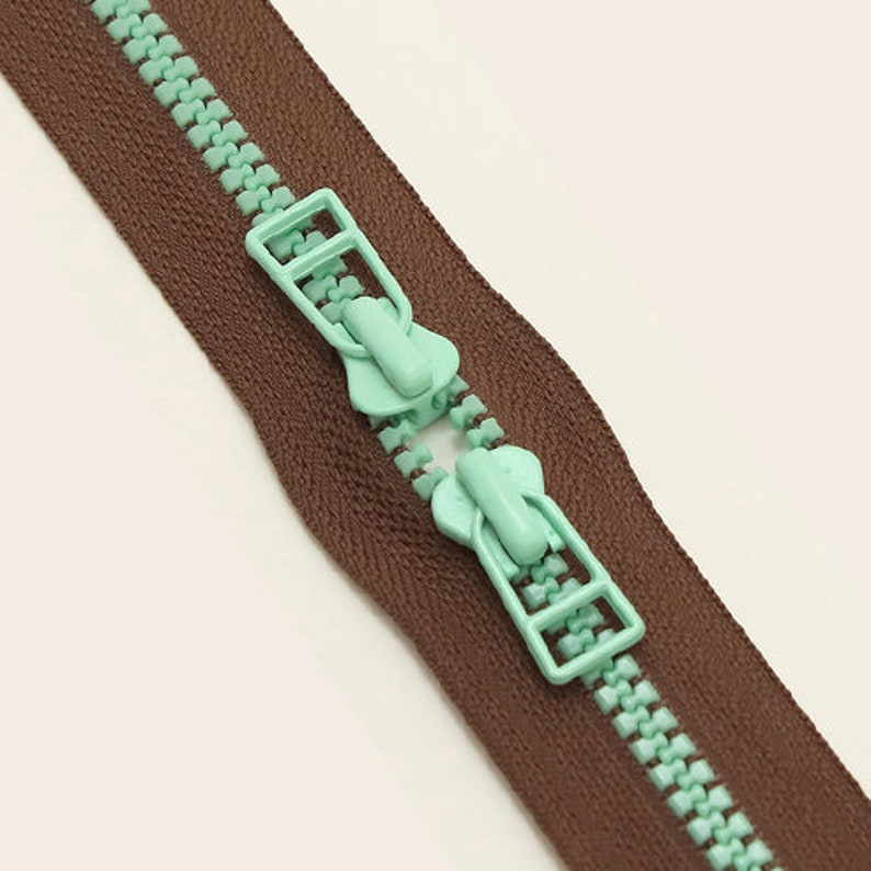 May include: A brown zipper with a mint green zipper pull. The zipper is closed and the pull is in the center of the zipper.