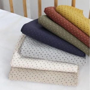 May include: A stack of fabric in various colors, including cream, beige, navy, olive green, rust, and yellow. Each fabric has a small, repeating floral pattern in black. The fabrics are neatly folded and stacked on top of each other.
