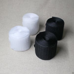 May include: Four rolls of hook and loop tape, two white and two black. The tape is rolled up and ready to be used for crafts, sewing, or other projects.