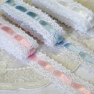 May include: Three white lace trims with different coloured satin ribbon accents. The trims feature a delicate lace pattern with oval-shaped satin ribbon accents in pink, light blue, and white.
