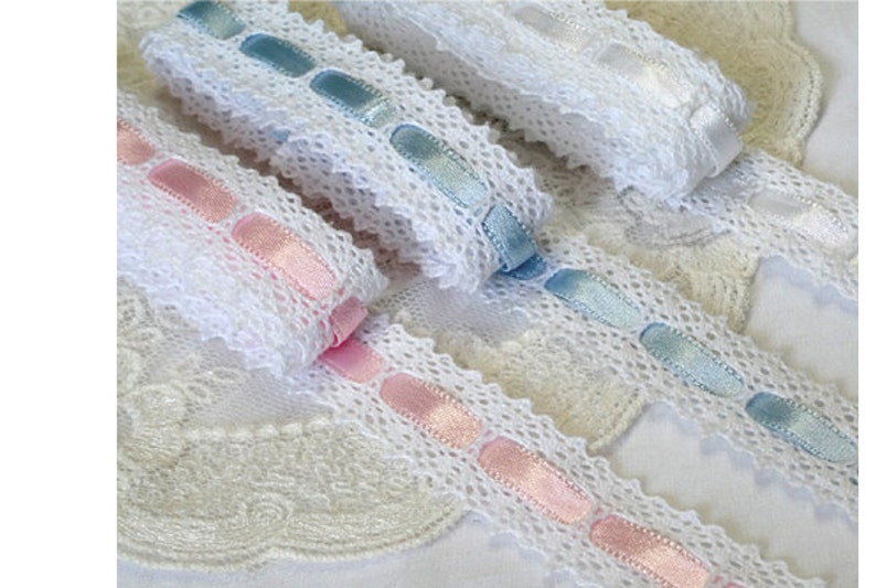 May include: Three white lace trims with different coloured satin ribbon accents. The trims feature a delicate lace pattern with oval-shaped satin ribbon accents in pink, light blue, and white.