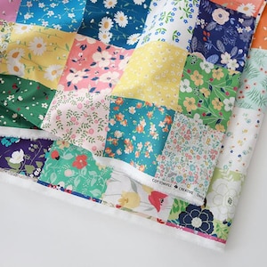 May include: A fabric sheet featuring a patchwork design of various floral patterns in colors including yellow, pink, green, blue, and white. The fabric displays a repeating grid of squares with diverse botanical prints and the text COTTONVILL CREATIVE Design.