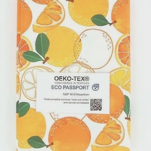 May include: A notebook featuring a pattern of oranges and orange slices on a white background. The notebook has a label with the text "OEKO-TEX® CONFIDENCE IN TEXTILES ECO PASSPORT".