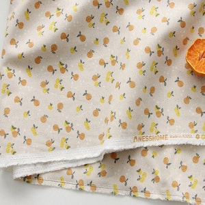 May include: Beige fabric with a repeating pattern of small orange and yellow citrus fruits with green leaves. The fabric has a white border and the text "NESSHOME Made in Korea" is visible in the bottom right corner.