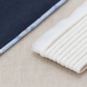 Pode incluir: Close-up de uma pilha de meias brancas dobradas ao lado de um tecido azul marinho com uma borda estampada floral. As meias estão cuidadosamente arrumadas, e o tecido tem uma borda delicada, azul claro e floral.