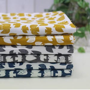 Peut inclure: Une pile de tissus pliés avec un motif d'oiseaux répété. Les tissus sont de différentes couleurs, dont le blanc, le jaune moutarde, le gris et le bleu marine. Le motif d'oiseau est une silhouette stylisée simple.