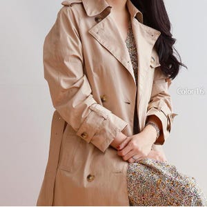 May include: A beige double-breasted trench coat featuring a wide collar, lapels, and buttoned cuffs with straps. The coat has dark brown buttons and is worn over a floral patterned garment. The text Color 16 is visible on the right side.