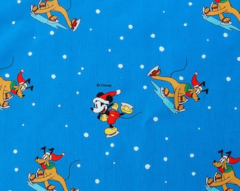 Puede incluir: Una tela azul con un patrón repetido de Mickey Mouse y Pluto patinando sobre hielo. Mickey Mouse lleva un gorro de Papá Noel rojo y blanco y Pluto lleva un gorro de Papá Noel rojo con una bufanda amarilla. El fondo es azul con copos de nieve blancos.