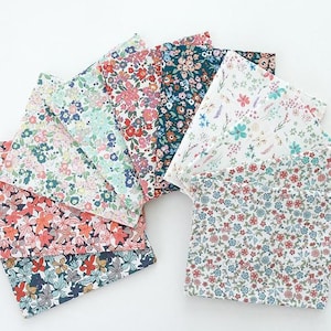 Peut inclure: Une collection de dix échantillons de tissu carrés disposés en éventail, chacun présentant des motifs floraux distincts avec diverses palettes de couleurs incluant des tons de rouge, bleu, vert, rose et blanc sur un fond clair.