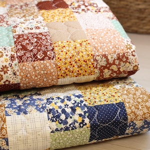 Pu&ograve; includere: Una trapunta patchwork composta da vari quadrati di tessuto nelle tonalit&agrave; del marrone, giallo, blu e verde. La trapunta presenta diversi motivi floreali, a pois e a griglia, con linee di cucitura visibili che collegano ogni quadrato.