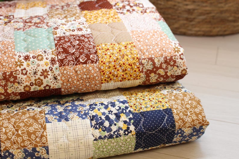 Pu&ograve; includere: Una trapunta patchwork composta da vari quadrati di tessuto nelle tonalit&agrave; del marrone, giallo, blu e verde. La trapunta presenta diversi motivi floreali, a pois e a griglia, con linee di cucitura visibili che collegano ogni quadrato.
