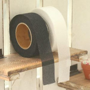 May include: Two rolls of tape, one black and one white, are displayed on a wooden shelf. The black tape is textured and has a strip extending downward. The white tape is smooth. The shelf is part of a decorative display.