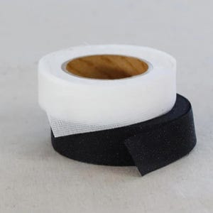 May include: A roll of white mesh ribbon sits atop a roll of black ribbon. The white ribbon is partially unrolled, revealing a brown cardboard core. The ribbons are likely used for crafting or decorative purposes.