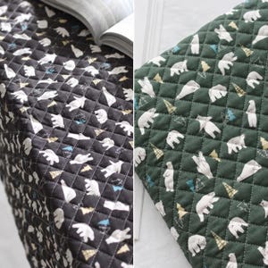 Puede incluir: Una tela acolchada con un patrón repetitivo de osos polares blancos y pequeños árboles triangulares en tonos dorados y azules. El textil está disponible en dos colores, uno con fondo negro y otro con fondo de color verde bosque oscuro.