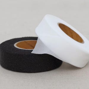 May include: Two rolls of tape, one black and one white, are displayed. The black roll has a textured surface, while the white roll is smooth. Both rolls have a brown core.
