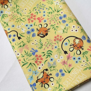 Op de afbeelding: Een gele stof met een herhalend patroon van ronde oranje wezens met lange staarten, kleine blauwe strikjes en diverse wilde bloemen in wit, blauw en roze. De tekst "POCKET MONSTERS" is in het wit langs de randen van de stof gedrukt.