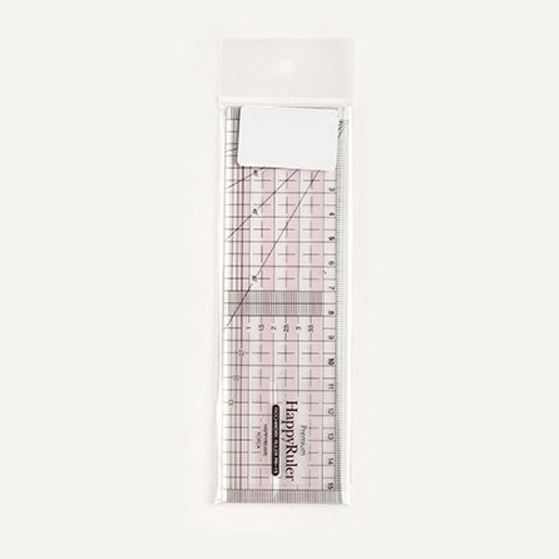 Puede incluir: Una regla Happy Ruler de pl&aacute;stico transparente en una funda de pl&aacute;stico transparente. La regla tiene l&iacute;neas de cuadr&iacute;cula rosas y medidas en cent&iacute;metros hasta 38 cm. Una etiqueta blanca est&aacute; adherida a la parte superior de la funda. La regla es para coser.