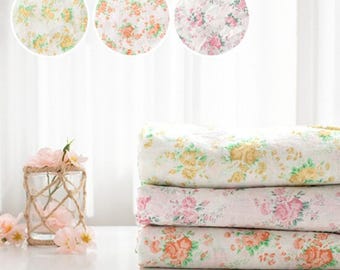 May include: Three folded floral patterned blankets in white, pink, and orange. The blankets are stacked on top of each other. Above the blankets are three circular floral patterns. A glass vase with flowers is on the left.
