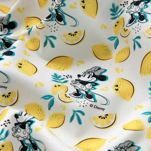 Puede incluir: Tela blanca con un patr&oacute;n repetido de personajes de dibujos animados de Minnie Mouse en blanco y negro y limones amarillos. La tela tiene un dise&ntilde;o de hojas verde y azul claro. El texto "&copy; Disney" est&aacute; impreso en la tela.
