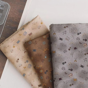 Peut inclure: Trois pièces de tissu pliées en beige, marron et gris, chacune présentant un motif répétitif d'icônes liées à la couture, notamment de petits ciseaux, des bobines de fil, des boutons, des épingles à nourrice, des machines à coudre et des brindilles.