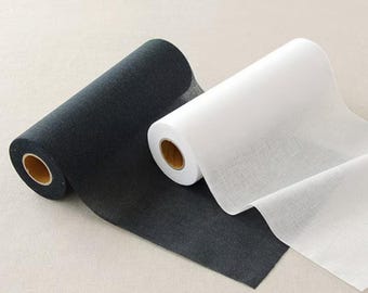 May include: Two rolls of fabric, one black and one white, are shown. The black roll is partially unrolled, displaying a textured surface. The white roll is also partly unrolled, revealing a smooth, translucent material. Both rolls have a cardboard core.