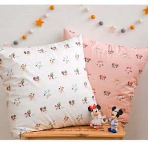 May include: Two white and pink pillowcases with a repeating pattern of Mickey Mouse and friends. The pillowcases are on a wooden surface with two small Mickey Mouse figurines.
