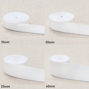 May include: Four rolls of white elastic band in different widths: 15mm, 20mm, 25mm, and 40mm. The elastic bands are rolled up and laid out on a beige fabric background.