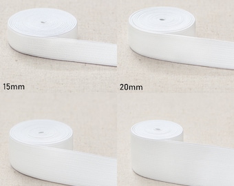 May include: Four rolls of white elastic band in different widths: 15mm, 20mm, 25mm, and 40mm. The elastic bands are rolled up and laid out on a beige fabric background.