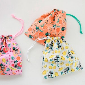 Puede incluir: Tres bolsas de cord&oacute;n con diferentes patrones de frutas. La primera bolsa es rosa con fondo blanco y presenta un patr&oacute;n de frutas rosas y amarillas, hojas verdes y personajes de Mickey Mouse. La segunda bolsa es naranja con fondo blanco y presenta un patr&oacute;n de rodajas de naranja y personajes de Mickey Mouse. La tercera bolsa es blanca con fondo amarillo y presenta un patr&oacute;n de limones y personajes de Mickey Mouse.