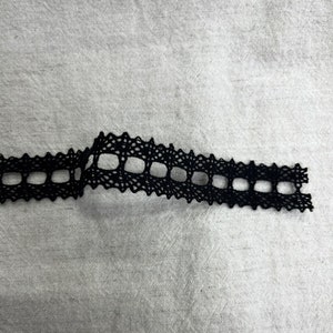 May include: Black lace trim with a square pattern. The trim is approximately 2.5 cm wide.
