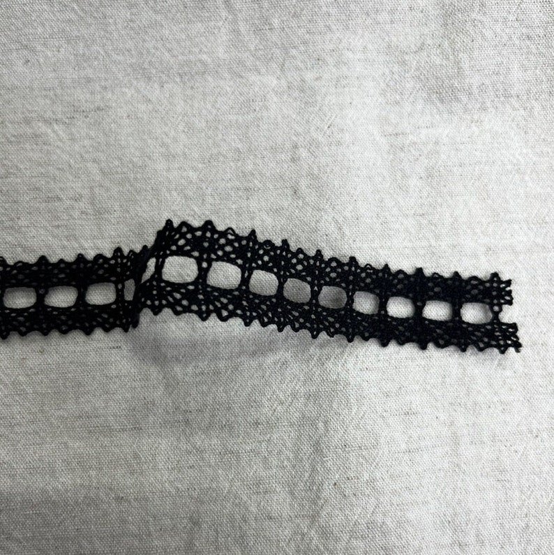 May include: Black lace trim with a square pattern. The trim is approximately 2.5 cm wide.