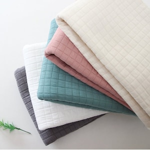 Pode incluir: Quatro tecidos acolchoados de cores diferentes, empilhados uns sobre os outros. As cores são branco, rosa claro, azul-petróleo e cinza.