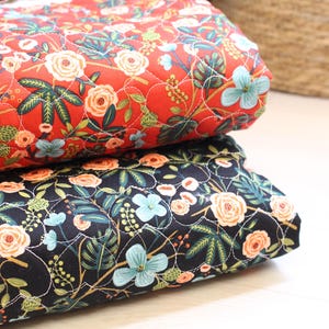 Pu&ograve; includere: Due pezzi di tessuto trapuntato piegati impilati l'uno sull'altro. Il pezzo superiore &egrave; rosso con un motivo floreale di fiori azzurri e color pesca con foglie verdi. Il pezzo inferiore &egrave; nero con lo stesso motivo floreale e cuciture bianche.