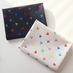 Peut inclure: Deux pièces de tissu pliées, une noire et une blanche, présentant toutes deux un motif répétitif de petites silhouettes de tête de Mickey Mouse multicolores en rouge, orange, jaune, vert, bleu et rose, avec le mot Disney écrit en petit.