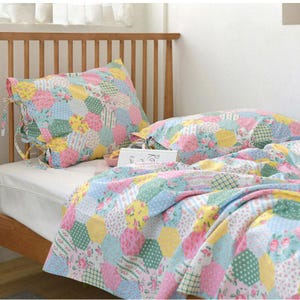 Peut inclure: Un lit avec un ensemble de courtepointe et d'oreillers en patchwork. La literie présente un mélange de couleurs pastel, dont le rose, le jaune et le bleu, avec des motifs floraux et géométriques. L'oreiller a des attaches.