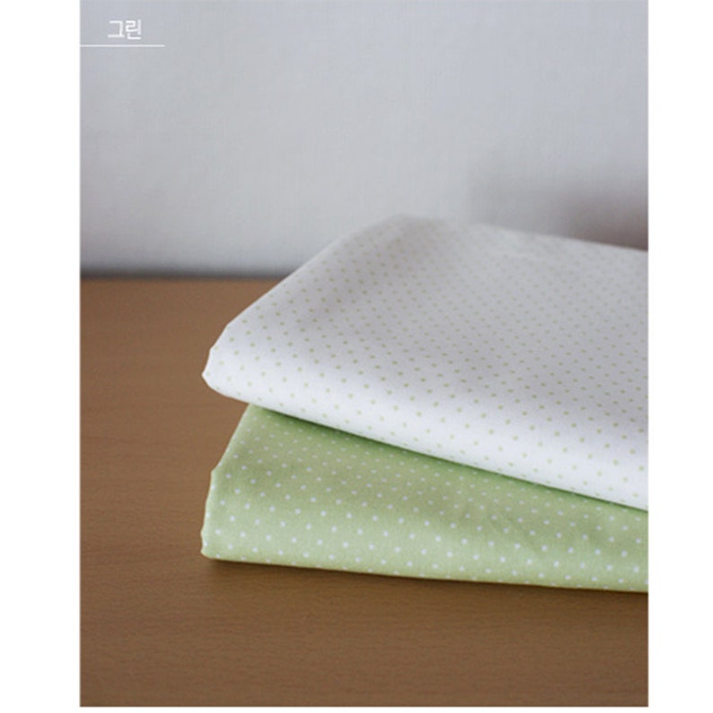 May include: Two folded pieces of fabric stacked on top of each other. The top piece is white with small light green polka dots, and the bottom piece is light green with small white polka dots. The text "그린" is visible in the top left corner.