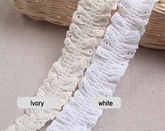 Peut inclure: Deux morceaux de dentelle en coton blanc, l'un ivoire et l'autre blanc. La dentelle a un bord festonné et un motif délicat d'œillets.