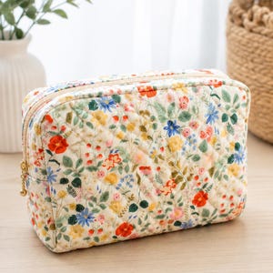 Pu&ograve; includere: Una trousse trapuntata rettangolare con base color crema e una stampa floreale di fiori rossi, gialli e blu intervallati da foglie verdi. La borsa presenta una chiusura a zip color oro con un piccolo cursore rotondo.