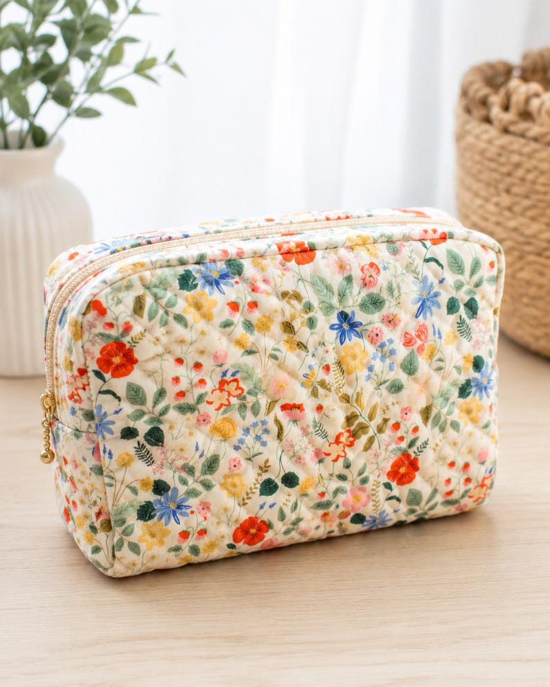 Pu&ograve; includere: Una trousse trapuntata rettangolare con base color crema e una stampa floreale di fiori rossi, gialli e blu intervallati da foglie verdi. La borsa presenta una chiusura a zip color oro con un piccolo cursore rotondo.