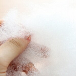 May include: Close-up of a handful of fluffy, white polyester fiberfill. The material is soft and cloud-like, ideal for stuffing pillows, cushions, or craft projects. The texture is airy and lightweight, perfect for adding volume and comfort.