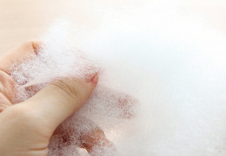 May include: Close-up of a handful of fluffy, white polyester fiberfill. The material is soft and cloud-like, ideal for stuffing pillows, cushions, or craft projects. The texture is airy and lightweight, perfect for adding volume and comfort.