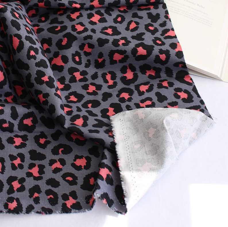 May include: Gray fabric with a pink leopard print pattern. The fabric is folded over, showing the white underside.