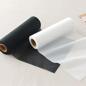 May include: Two rolls of fabric, one black and one white, are displayed. The black roll has a textured, speckled appearance, while the white roll is smooth and translucent. The rolls are partially unrolled, revealing the fabric's texture and color.