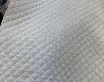 Puede incluir: Primer plano de una tela acolchada blanca con un patrón de diamante. La tela tiene una textura ligeramente rugosa y es perfecta para proyectos de manualidades.
