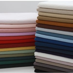 Peut inclure: Deux piles hautes et soignées de carrés de tissu pliés disposés côte à côte. La pile de gauche présente des nuances de blanc, rose, lavande, rouge, jaune, vert et noir. La pile de droite affiche des tons neutres, des bleus et des gris foncés.