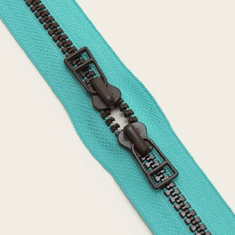 May include: A turquoise zipper with brown metal teeth and two brown plastic sliders.