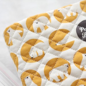 May include: A white fabric pouch with a quilted pattern featuring repeated images of polar bears in yellow circles. The pouch has a black label with the text "Polar Bear" in white.